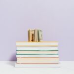 Stack of books with a stack of US dollar bills on top against a pastel background.