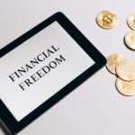 Tablet showing 'Financial Freedom' with gold bitcoins nearby, symbolizing cryptocurrency investment.