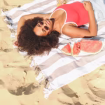 woman in spaghetti strap top lying on a towel on beach sand