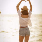 woman standing on beach showing heart sign